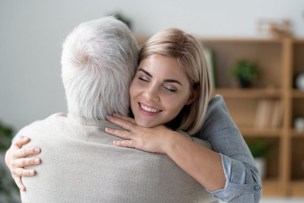 Dona jove i afectuosa feliç amb un somriure de dents abraçant el seu pare gran